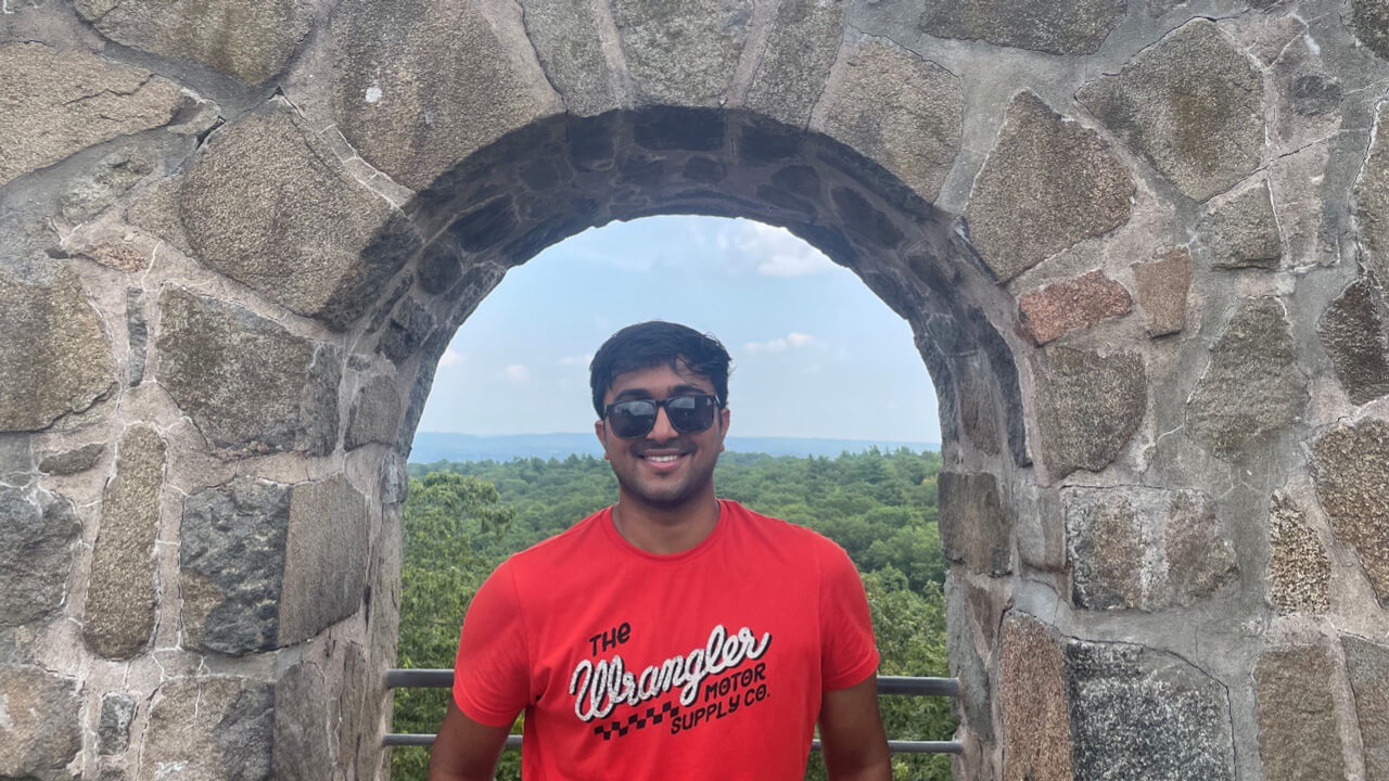 Maheep Achanta in a stone arch window that overlooks trees and the sky outside