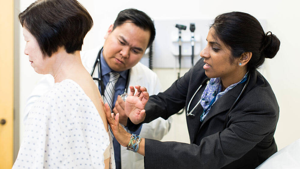 A medical student and professor examine the back of a standardized patient