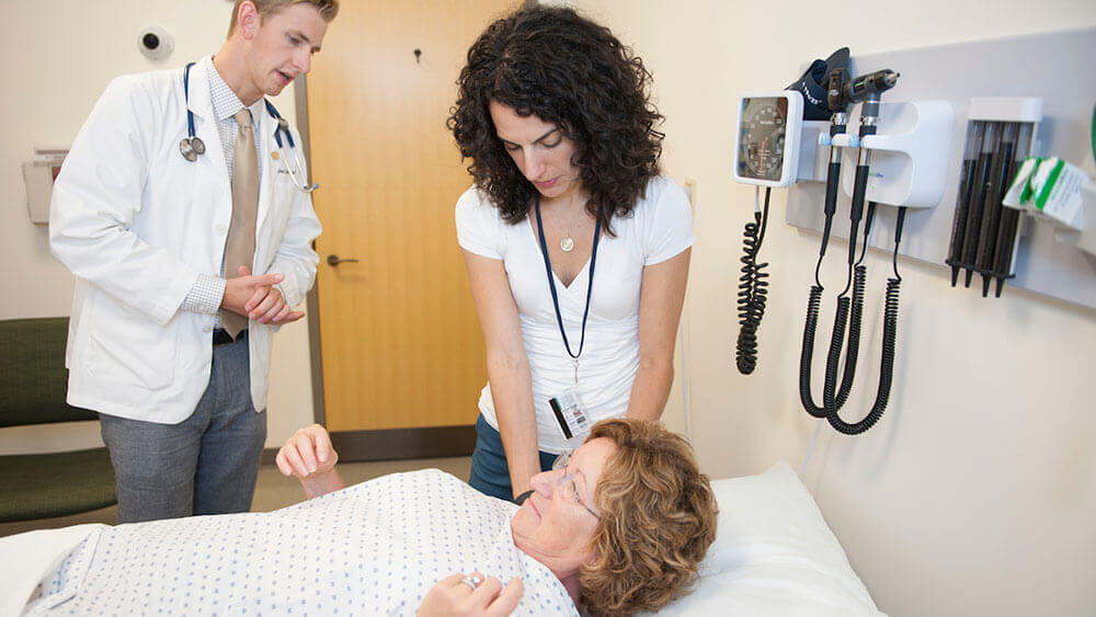 A medical student examining a patient in the Standardized Patient and Assessment Center under the guidance of a professor