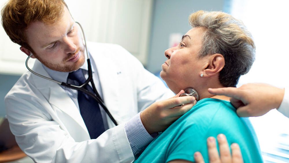 A medical student uses a stethoscope to hear the pulse of a patient